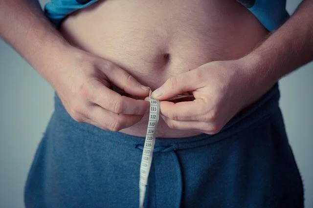 Persona con sobrepeso midiéndose la cintura abdominal con una cinta métrica.