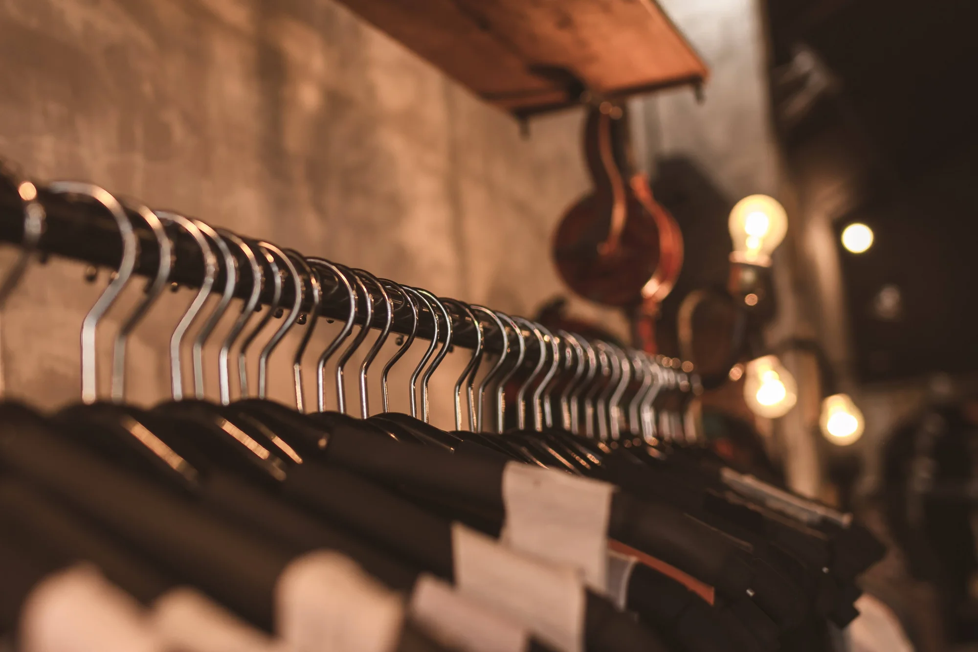 Fila de perchas metálicas vacías sobre un riel en una tienda con iluminación cálida de estilo industrial al fondo.