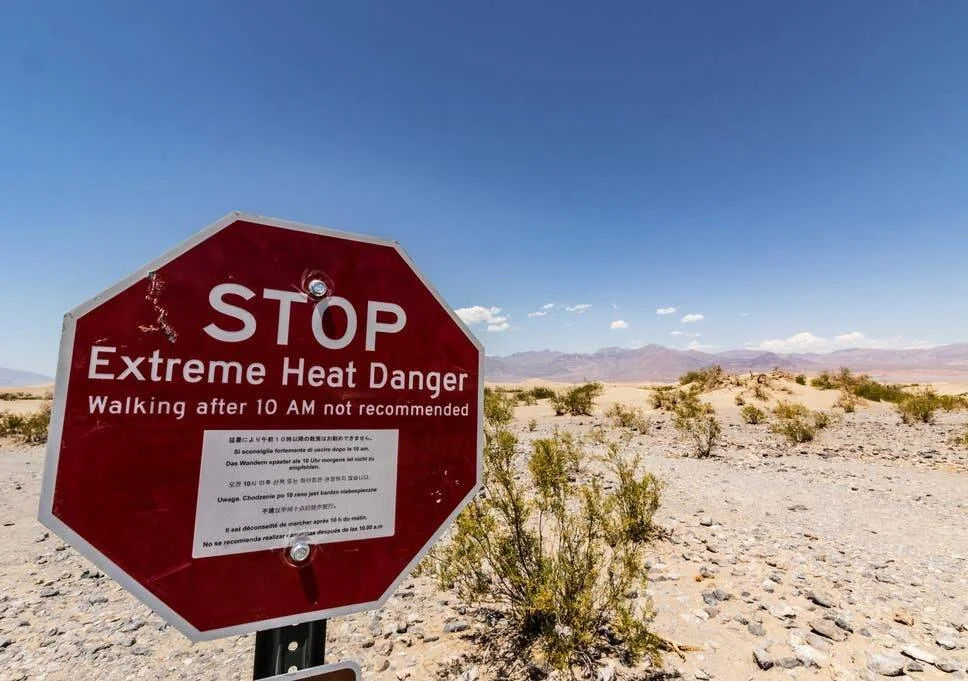 Señal roja octogonal en un desierto árido advierte 'Stop – Extreme Heat Danger' y desaconseja caminar después de las 10 AM.