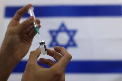 Manos preparan una jeringa con vacuna frente a la bandera de Israel.