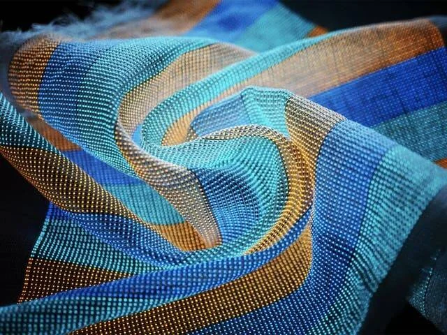 Tela de malla semitransparente con franjas en tonos azul, turquesa y dorado, enrollada en forma de espiral.