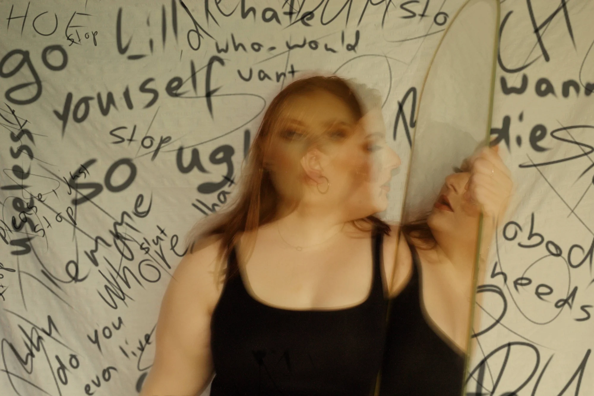 Retrato con efecto de movimiento de una mujer frente a una tela cubierta de insultos y mensajes de odio escritos a mano.