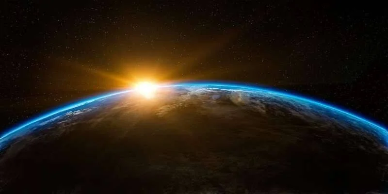 El sol sale sobre el horizonte curvo de la Tierra, iluminando la atmósfera azul contra el fondo estrellado del espacio.