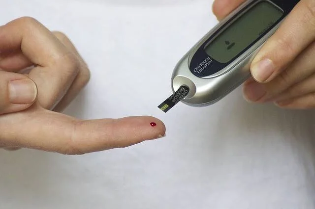 Persona aplicando tira reactiva de glucómetro en una gota de sangre del dedo para medir el nivel de azúcar.
