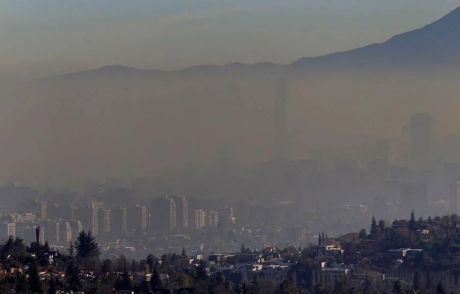 Vista panorámica de una ciudad con edificios y montañas casi ocultos por una densa capa de contaminación atmosférica.