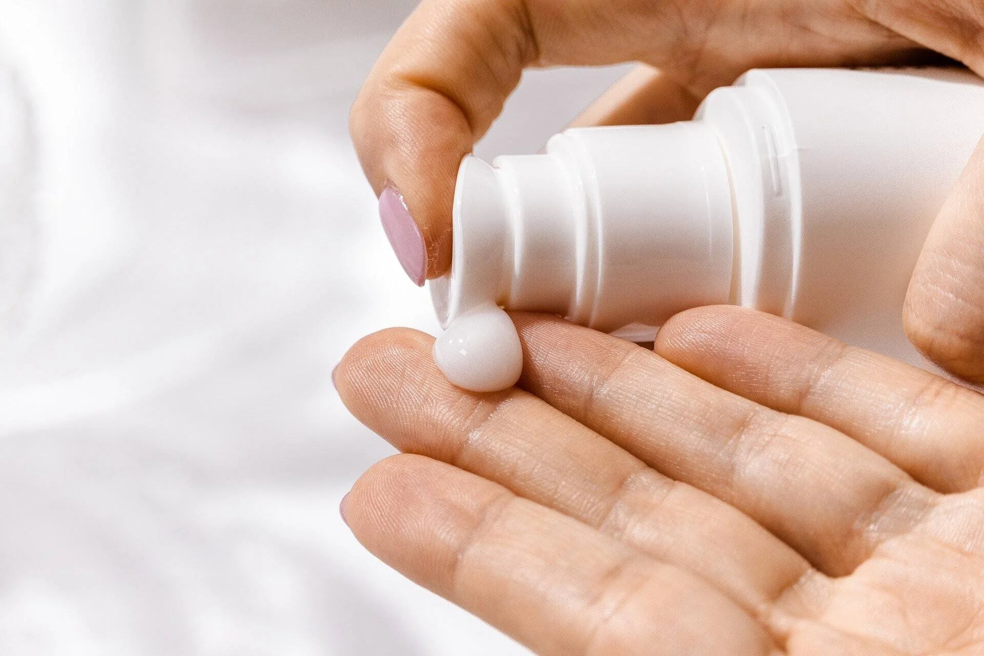 Una persona aplica una gota de crema blanca desde un envase dispensador sobre la palma de su mano.