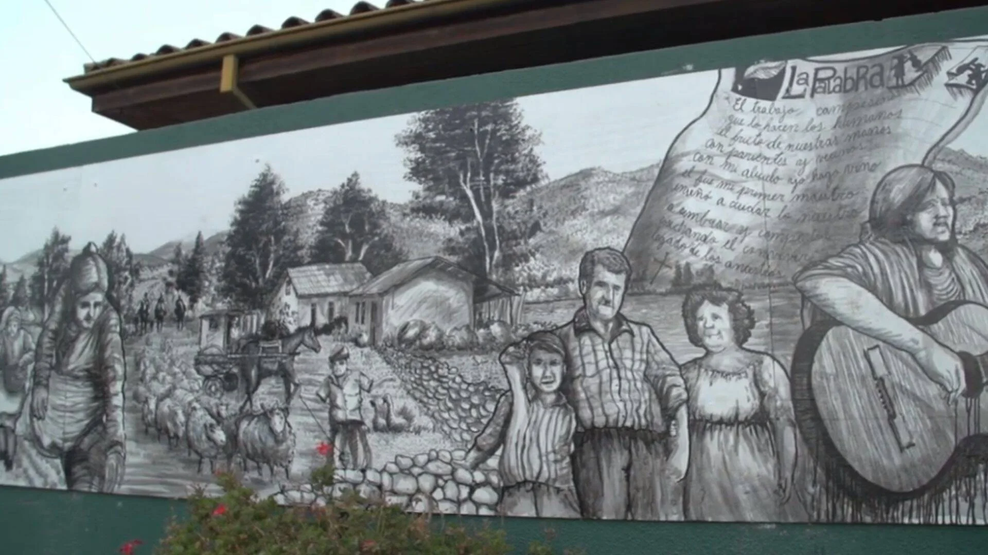 Mural en escala de grises que representa la vida campesina: familia rural, ovejas, casas y un texto poético sobre el trabajo del campo.