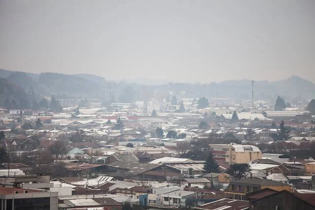 Vista panorámica de una ciudad con techos nevados envuelta en una densa capa de smog y neblina invernal.