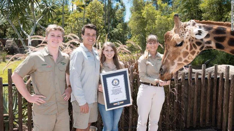 Cuatro personas en uniforme de guardabosques sostienen un certificado Guinness World Records frente a una jirafa en un zoológico.