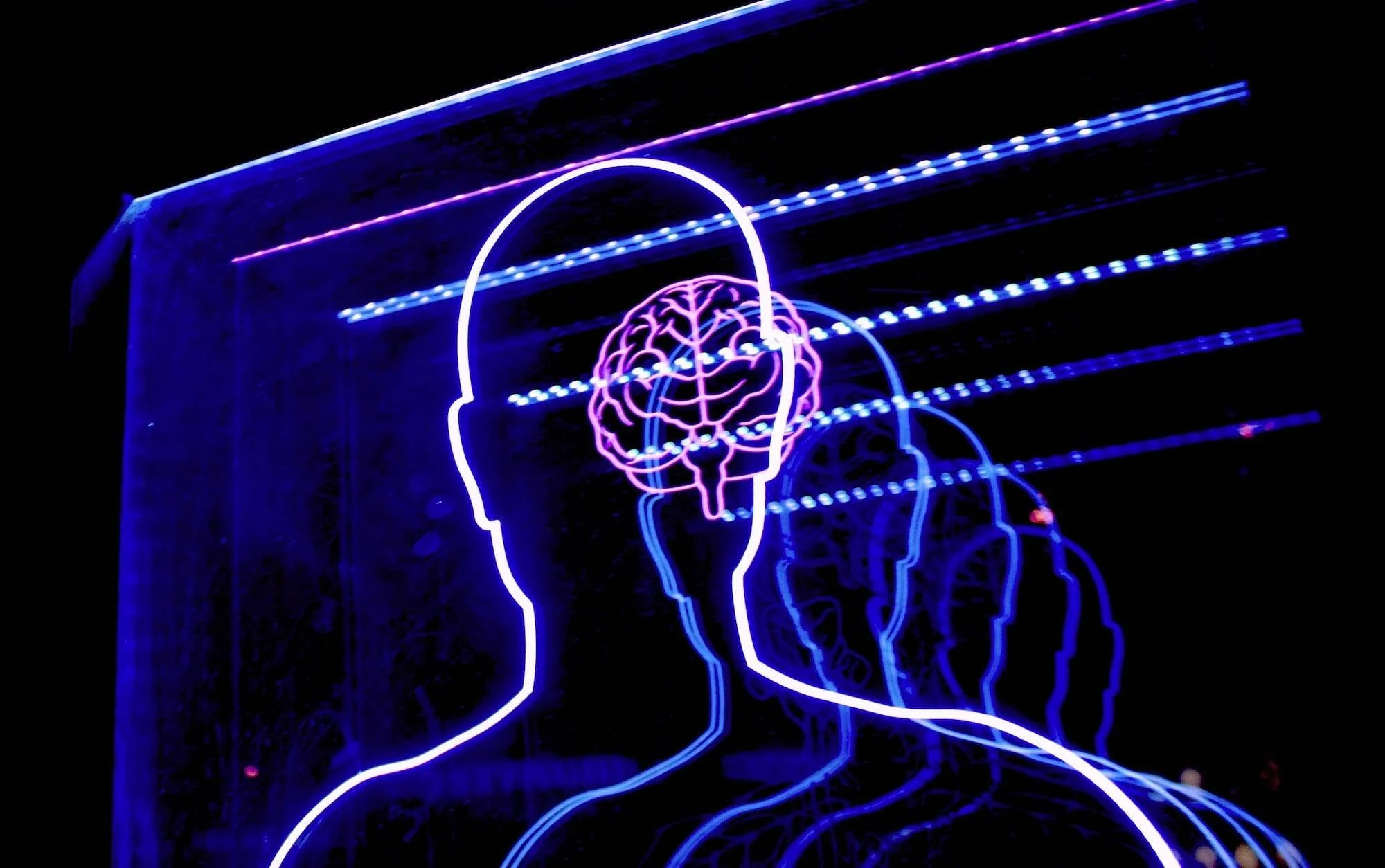 Silueta humana iluminada con luces de neón azul y blanco mostrando un cerebro en color rosa dentro del cráneo.