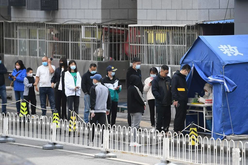 Grupo de personas con mascarilla hace fila en un puesto de pruebas COVID-19 en una calle de China.