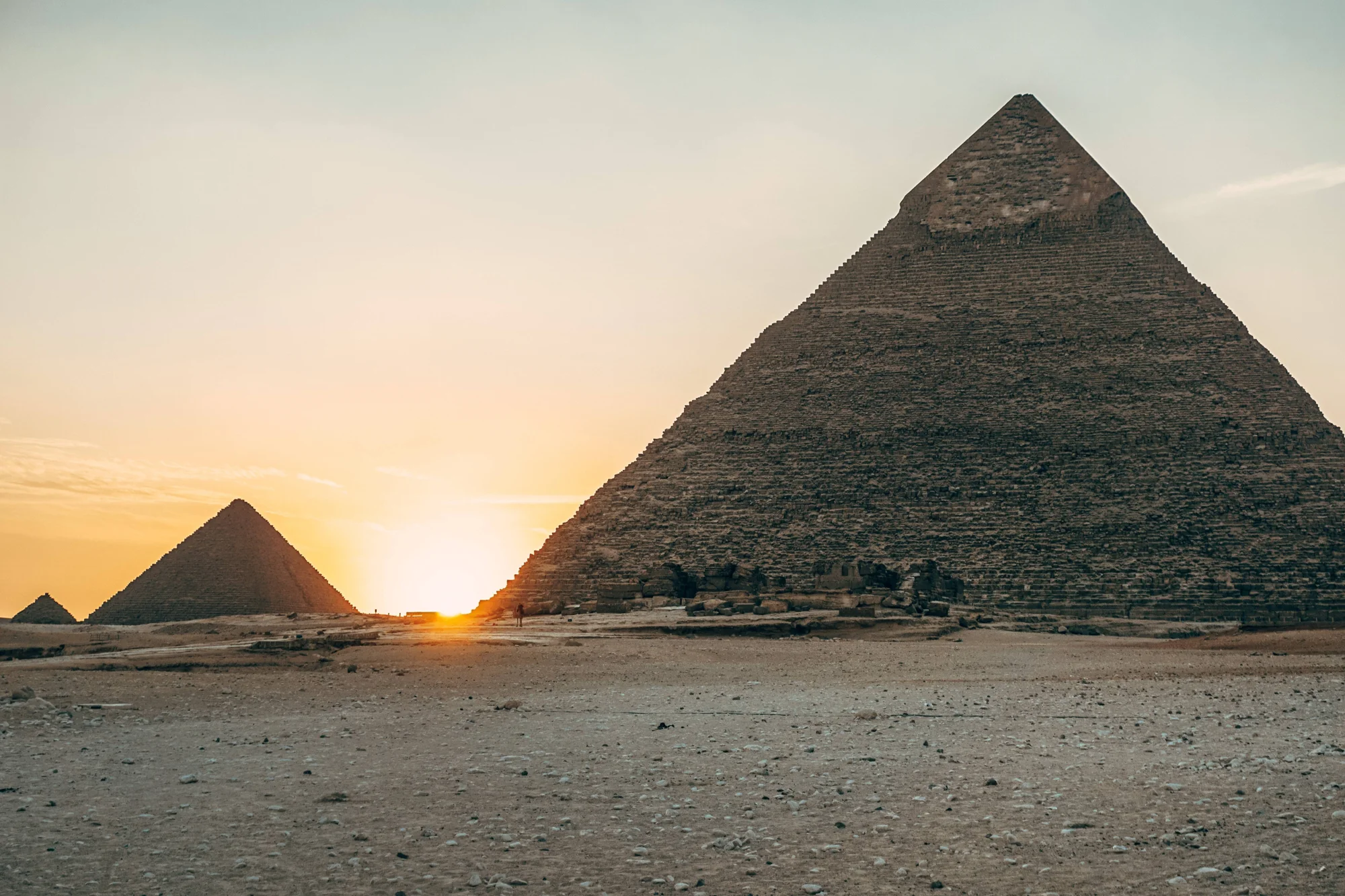 Las pirámides de Giza se recortan contra un cielo dorado al atardecer, con el sol poniéndose entre las estructuras sobre el desierto egipcio.