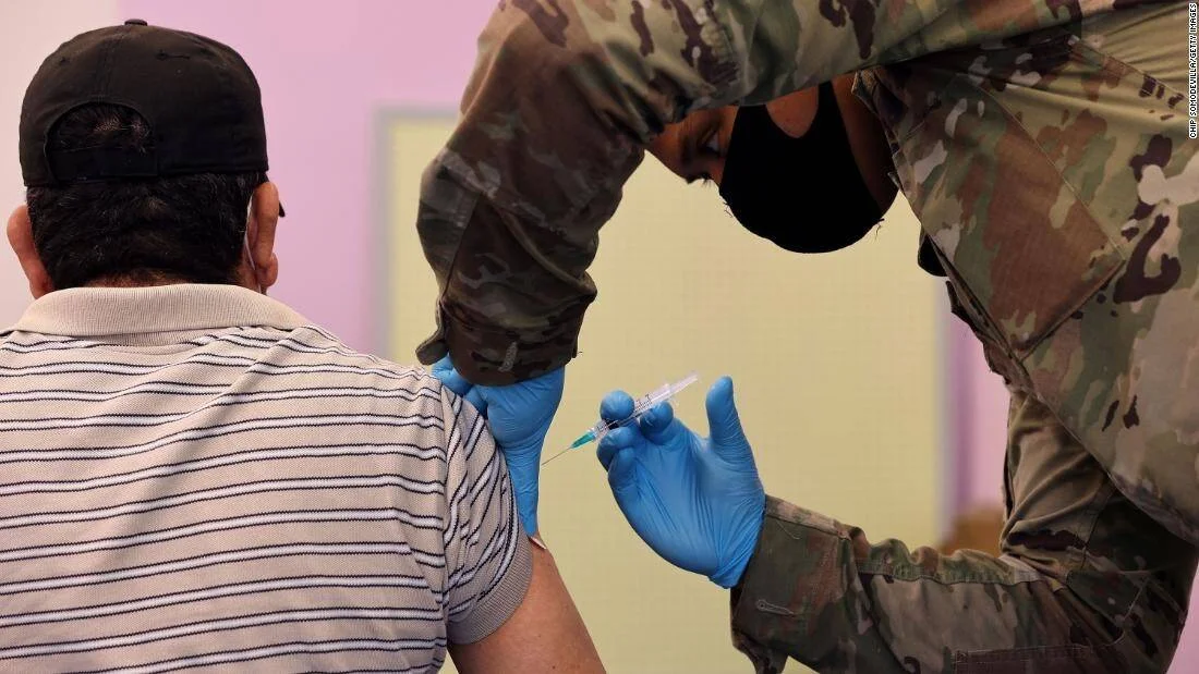 Personal militar con guantes aplica una inyección en el brazo de un hombre con mascarilla en un centro de vacunación.