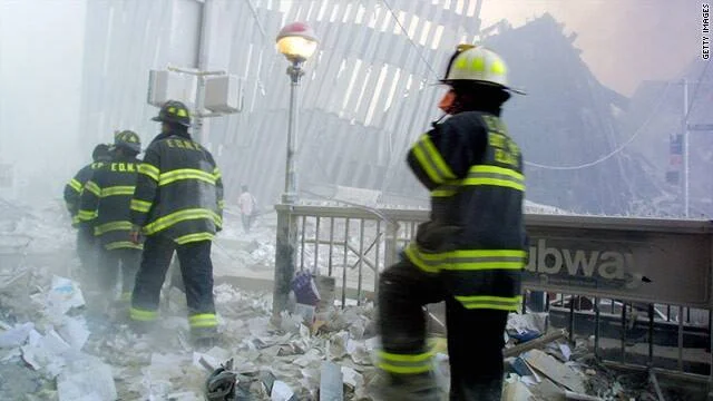 Bomberos caminan entre escombros y polvo denso en las inmediaciones del World Trade Center tras los ataques del 11 de septiembre de 2001.