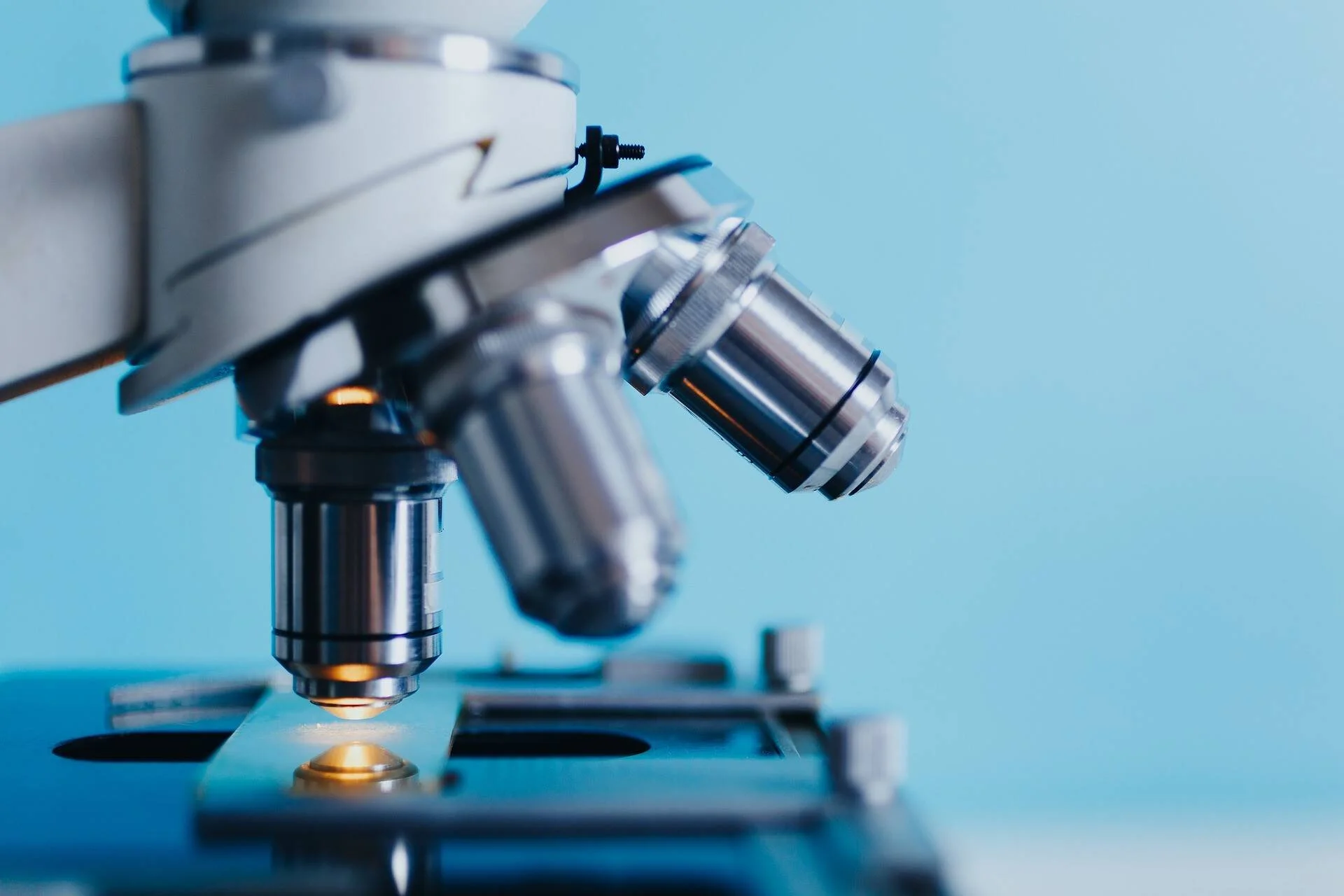 Primer plano de los objetivos metálicos de un microscopio óptico sobre fondo azul claro.