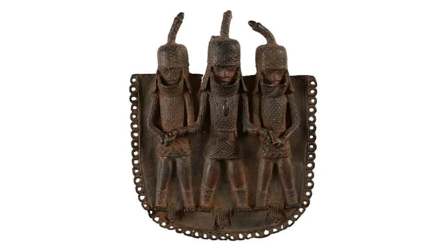 Placa de bronce del reino de Benín con tres figuras humanas con tocados, elaborada con técnica de relieve en metal oscurecido.