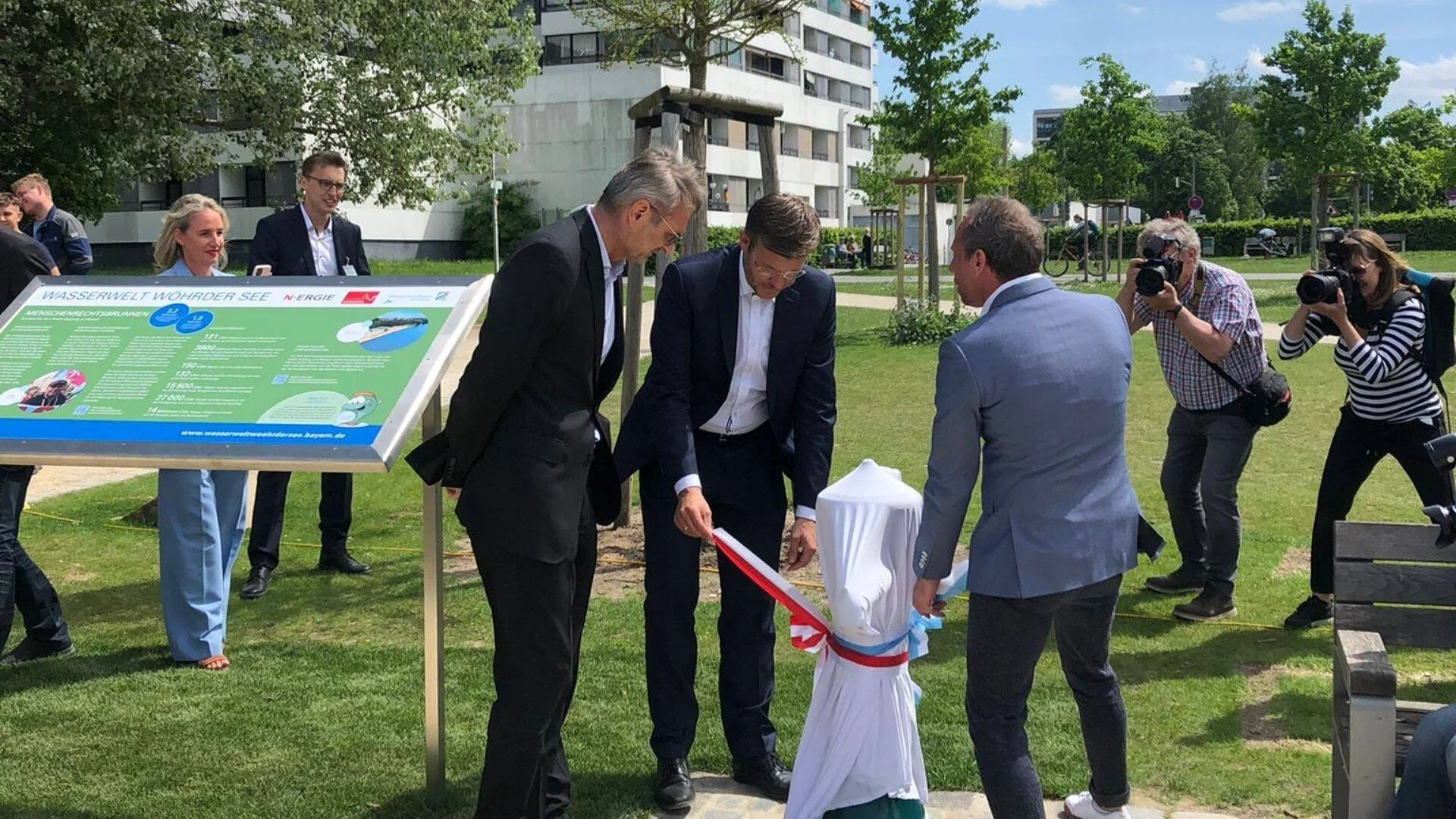 Tres hombres descubren una escultura cubierta durante la inauguración del proyecto Wasserwelt Wohrder See en un parque urbano.