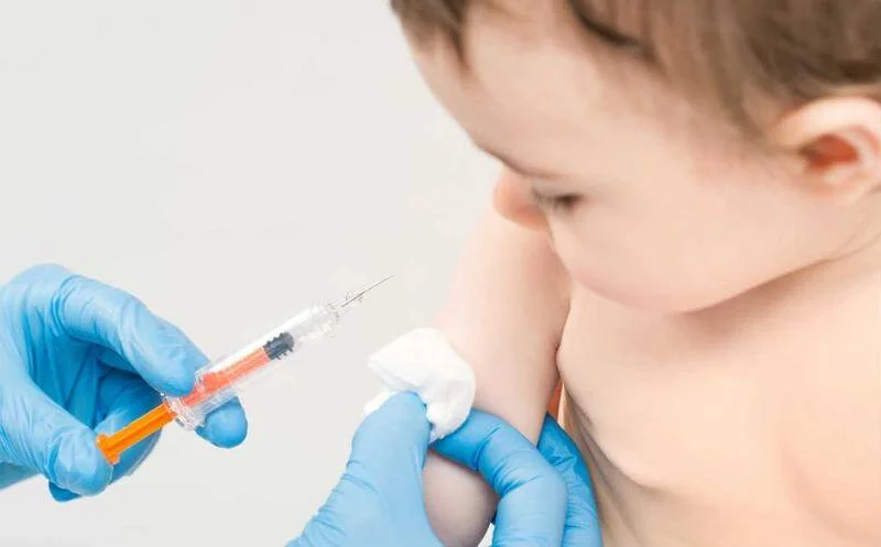 Profesional de salud con guantes aplica una vacuna en el brazo de un niño pequeño.
