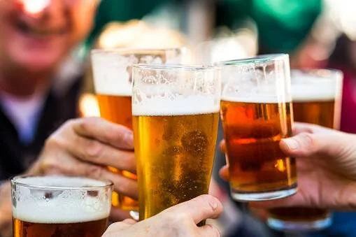 Varias personas chocan vasos de cerveza rubia en un brindis al aire libre.