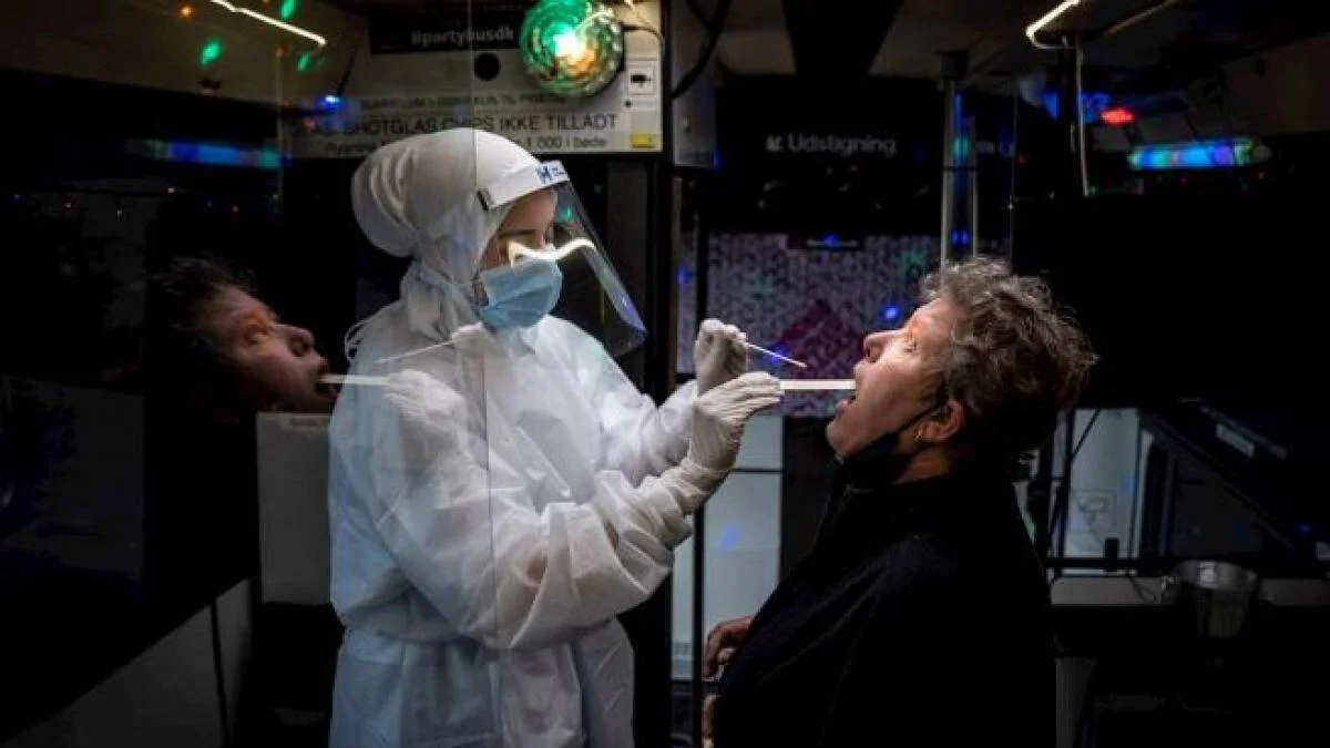 Profesional de salud con traje de protección realiza hisopado a una persona en un local de ambiente nocturno.