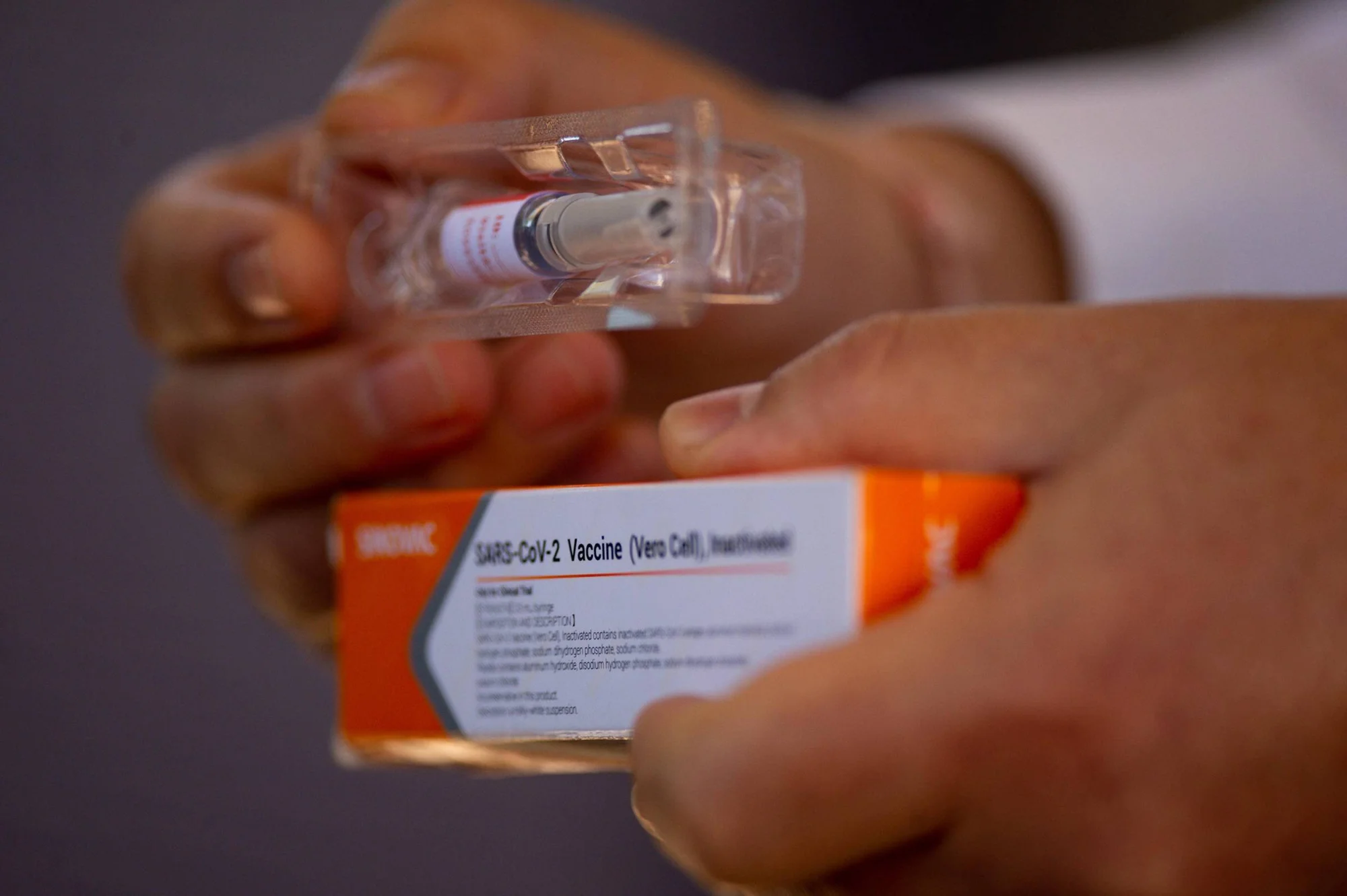 Manos sosteniendo un vial y la caja de la vacuna inactivada contra SARS-CoV-2 (Vero Cell) de Sinovac.