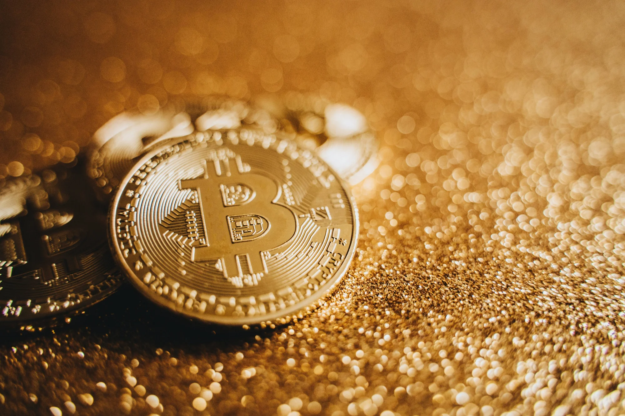 Moneda representativa de Bitcoin con el símbolo grabado, apoyada sobre una superficie de destellos dorados.
