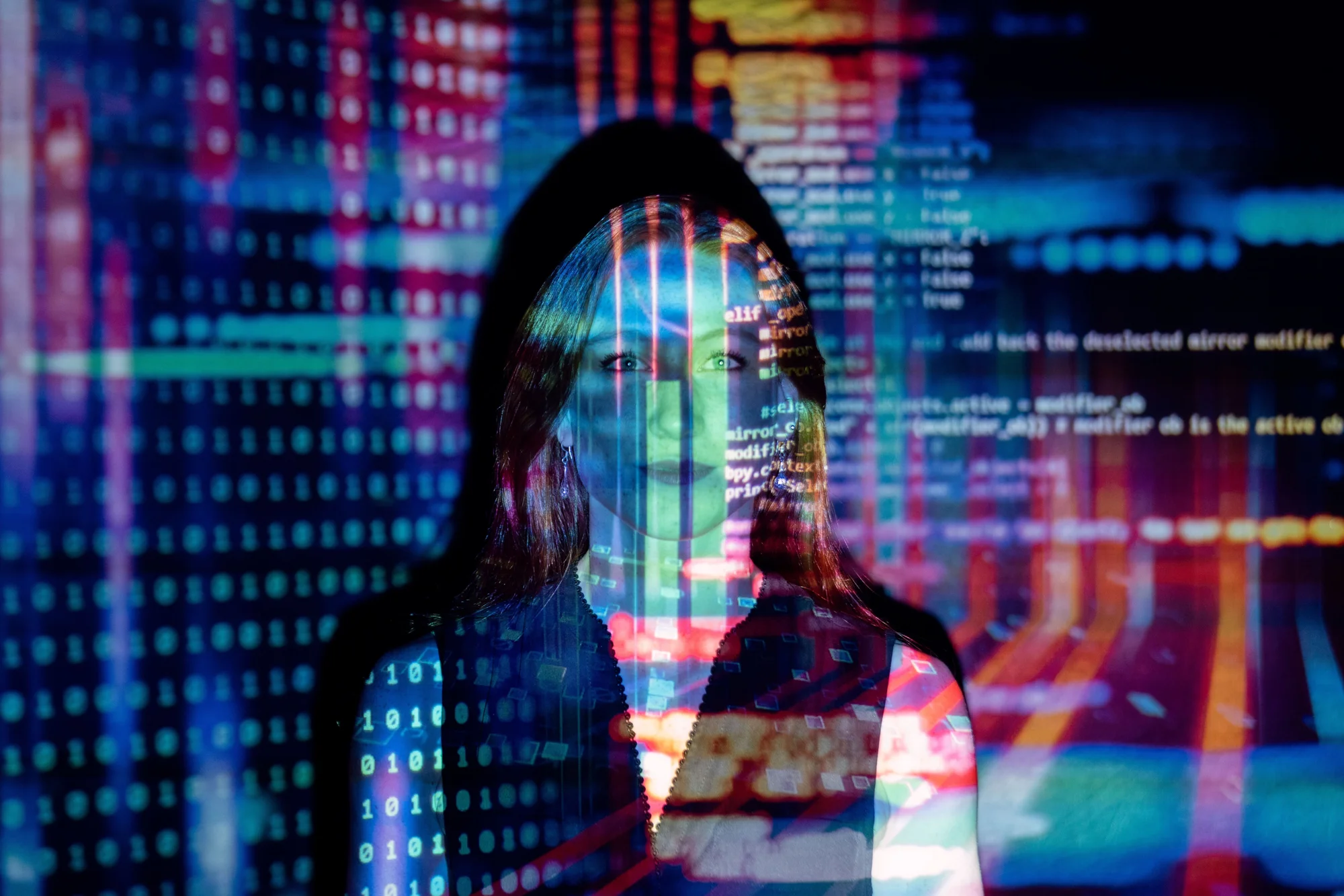 Mujer iluminada por proyecciones de código binario y líneas de programación en colores azul y rojo, evocando tecnología e inteligencia artificial.