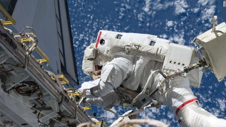 Astronauta con traje espacial blanco realiza una caminata extravehicular con la Tierra de fondo.