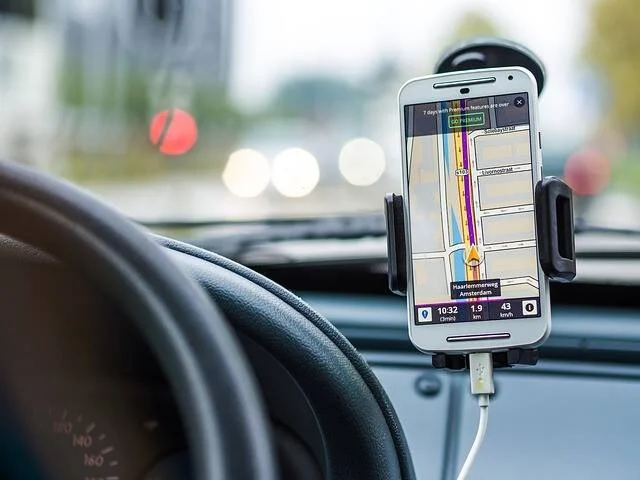 Teléfono celular montado en el tablero de un auto mostrando una aplicación de navegación GPS con mapa de rutas.