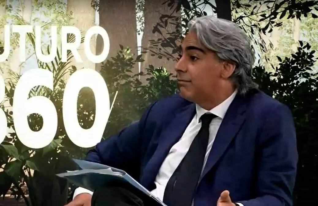 Hombre de traje azul y corbata negra participando en un foro denominado Futuro 360, con documentos en mano.