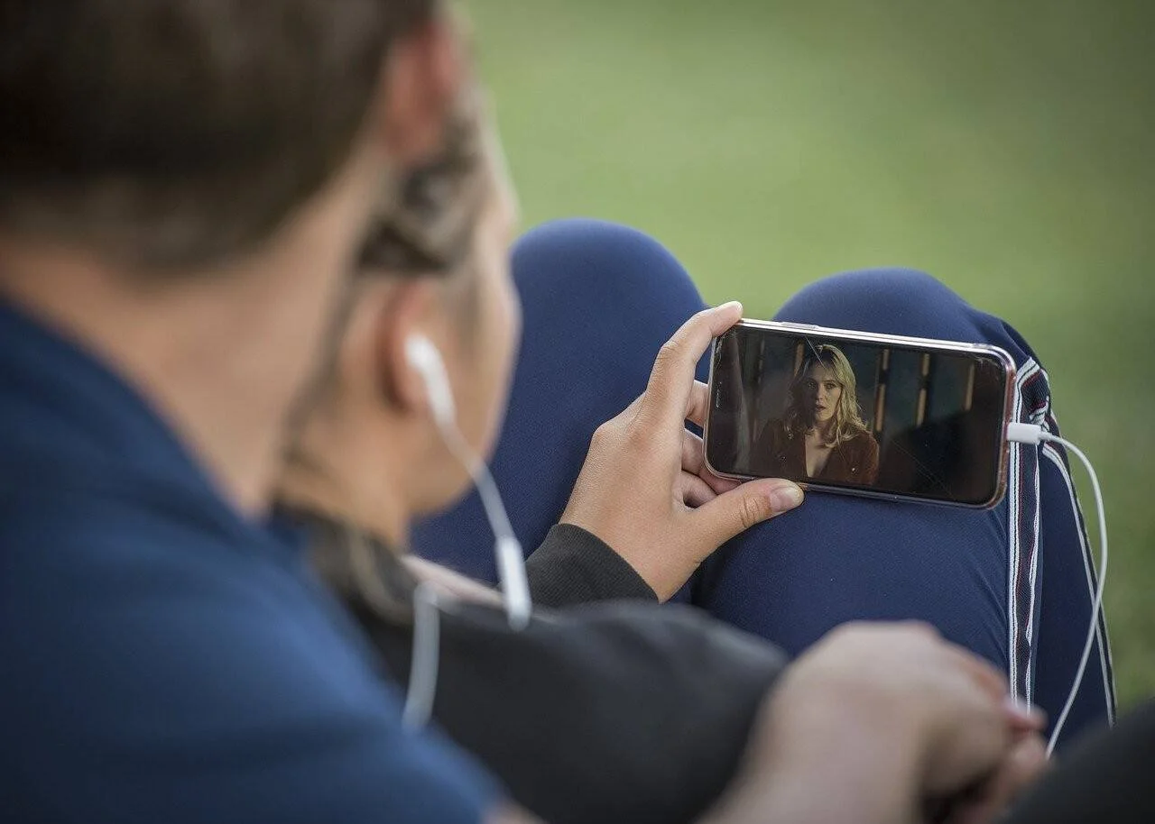 Joven con auriculares mira un video en su teléfono móvil mientras está sentado al aire libre.