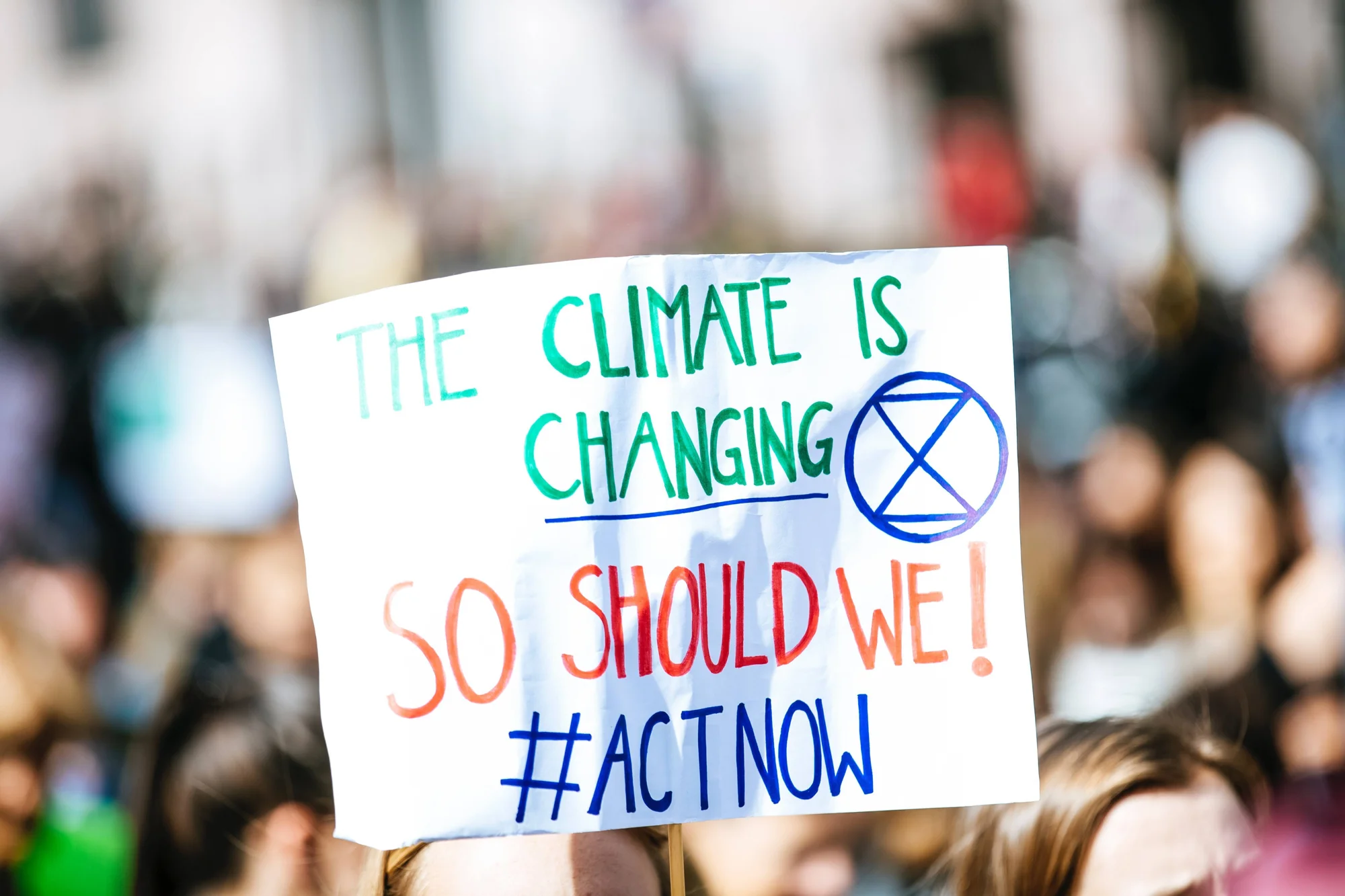 Cartel en una manifestación con el mensaje 'The climate is changing, so should we! #ActNow' y el símbolo de Extinction Rebellion.