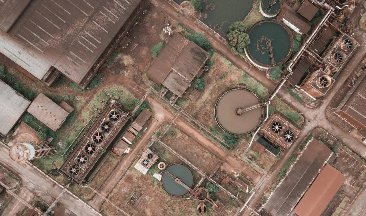 Vista desde dron de una planta industrial abandonada con tanques de sedimentación circular, galpones oxidados y maquinaria en desuso.