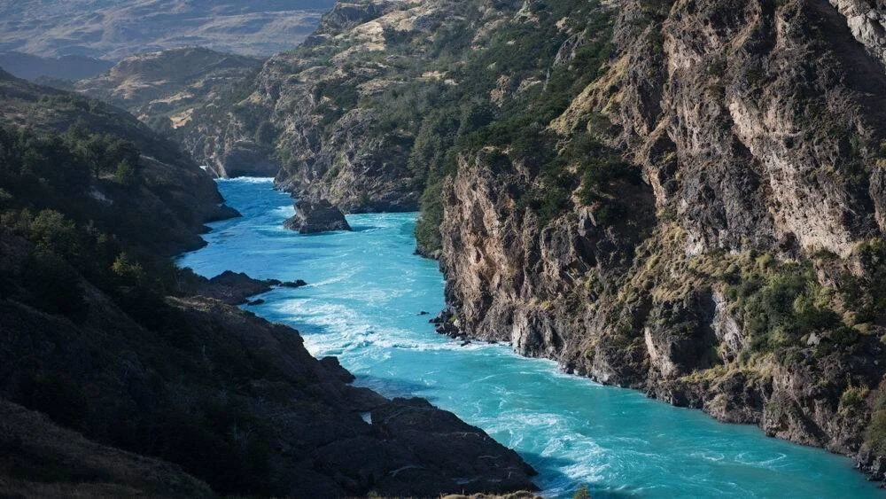 Río de aguas turquesas con rápidos discurre entre escarpados acantilados rocosos cubiertos de vegetación en la Patagonia.