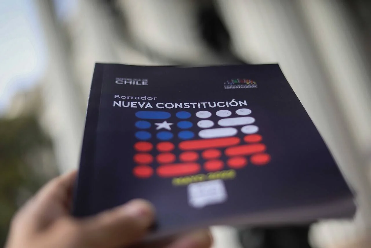 Una persona sostiene el borrador de la Nueva Constitución de la República de Chile con la bandera estilizada en la portada.