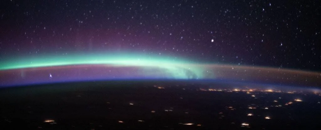 Aurora boreal con bandas de luz verde y púrpura sobre la curvatura de la Tierra, fotografiada desde el espacio con estrellas de fondo.