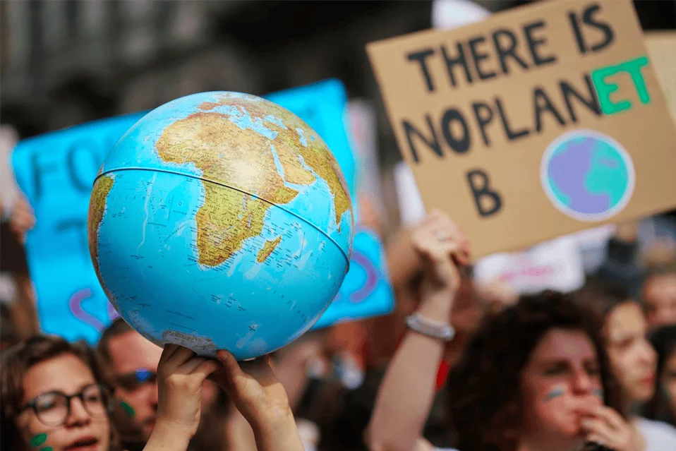 Manifestante sostiene un globo terráqueo en una marcha por el clima; al fondo se ve un cartel que dice 'There is no planet B'.