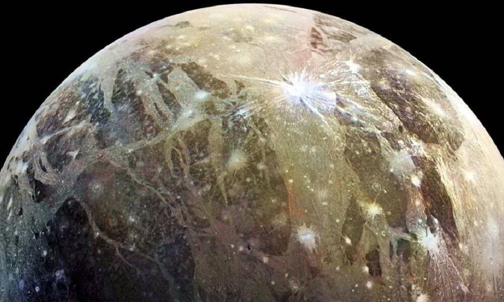 Vista cercana de una luna helada de Júpiter mostrando cráteres de impacto, fracturas y terreno variado sobre fondo negro del espacio.