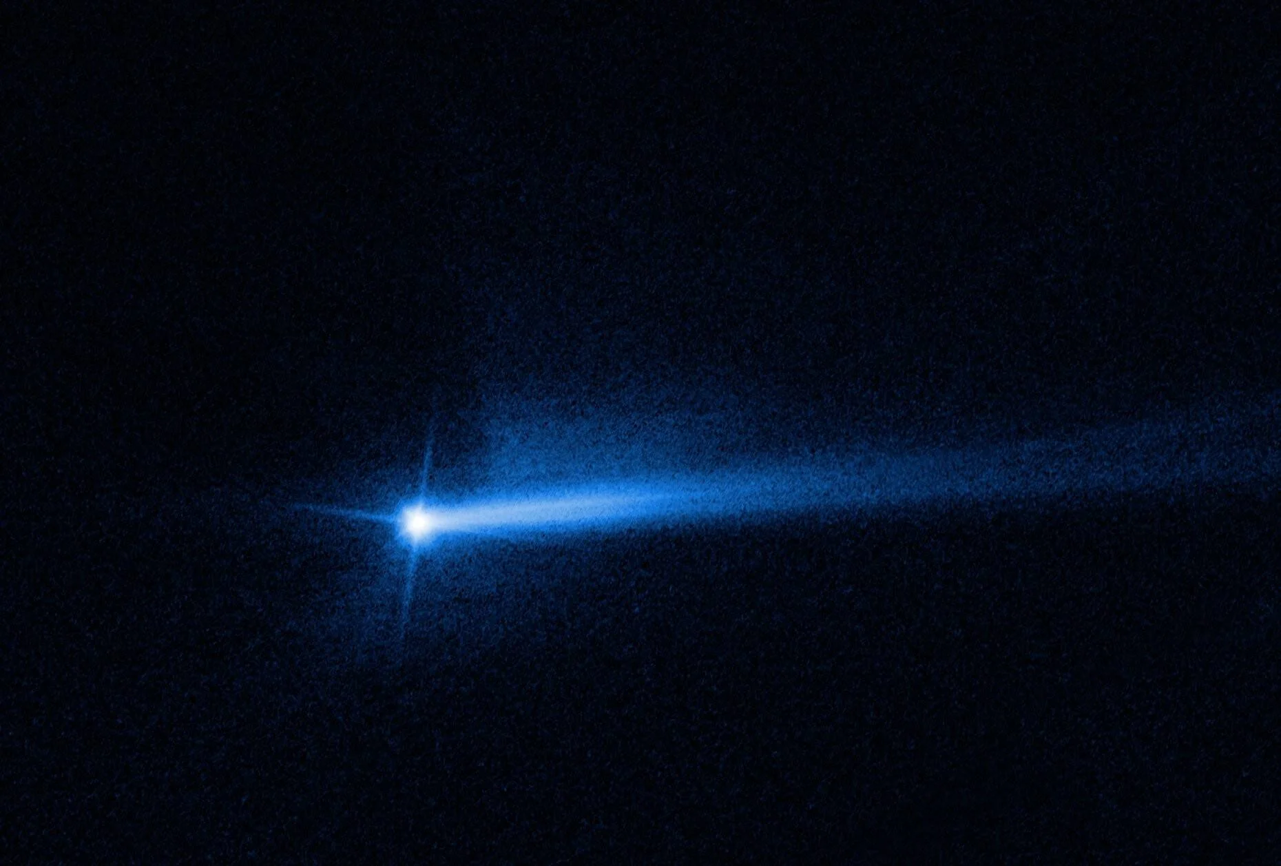Asteroide brillante con dos colas de polvo azuladas que se extienden hacia la derecha sobre el fondo oscuro del espacio.