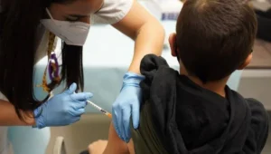 Una enfermera con mascarilla y guantes aplica una inyección en el brazo de un niño.