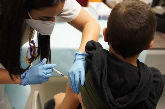 Una enfermera con mascarilla y guantes aplica una inyección en el brazo de un niño.
