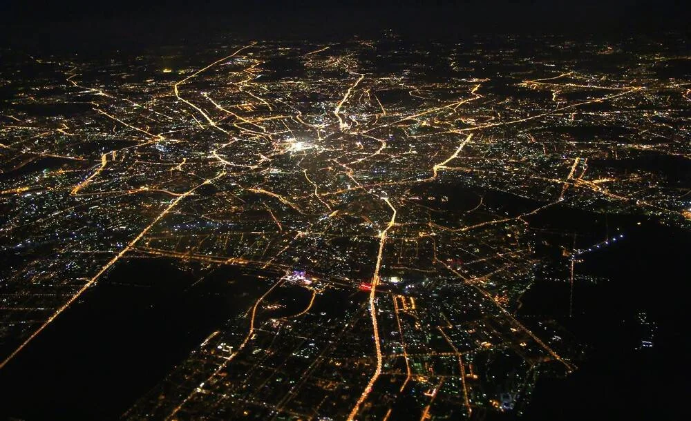 Gran ciudad vista desde el aire de noche, con avenidas y calles iluminadas que irradian desde el centro urbano.