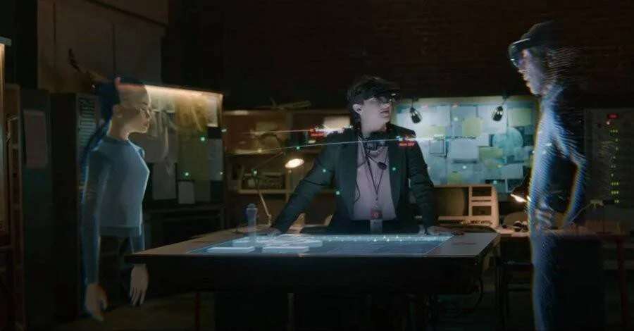 Persona con visor de realidad aumentada interactúa con dos avatares holográficos sobre una mesa de datos luminosa.