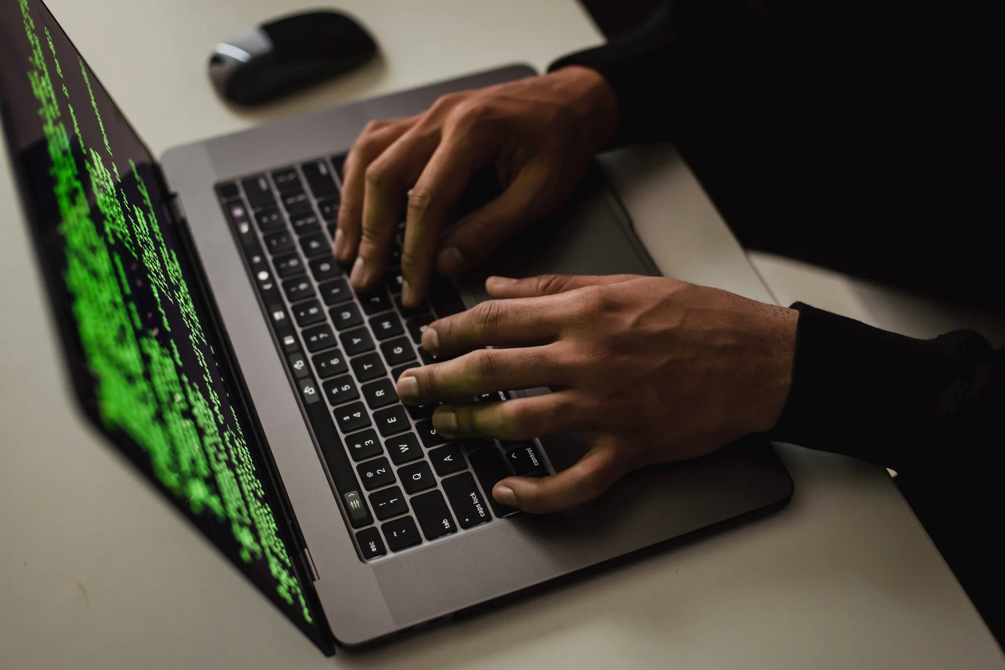 Persona escribiendo en una laptop con código verde en pantalla, evocando actividad de ciberataque o hacking.