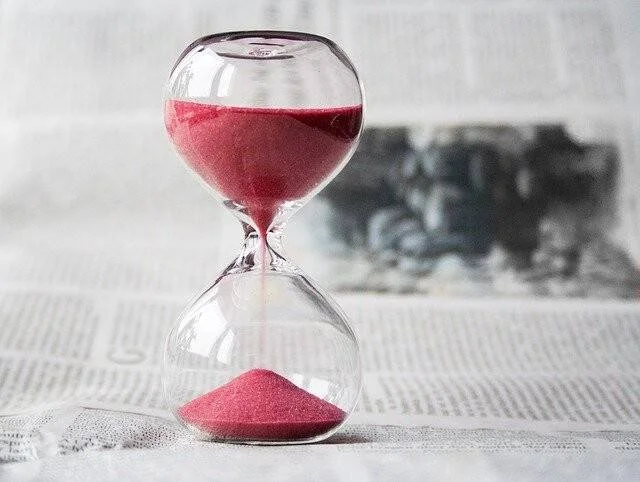 Reloj de arena con arena de color rosa fluyendo, apoyado sobre páginas de un periódico en blanco y negro.