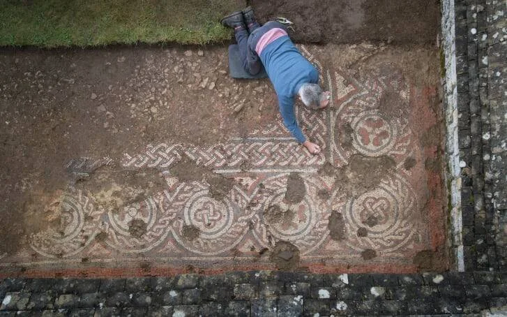 Vista aérea de un arqueólogo tumbado sobre un gran mosaico romano con motivos geométricos y entrelazados recién excavado.