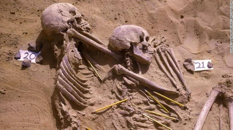 Dos esqueletos humanos etiquetados como 20 y 21 yacen en sedimento arenoso durante una excavación arqueológica.