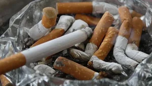 Cenicero de vidrio repleto de colillas de cigarrillos apagadas y ceniza.