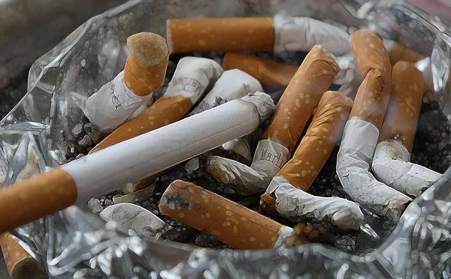 Cenicero de vidrio repleto de colillas de cigarrillos apagadas y ceniza.