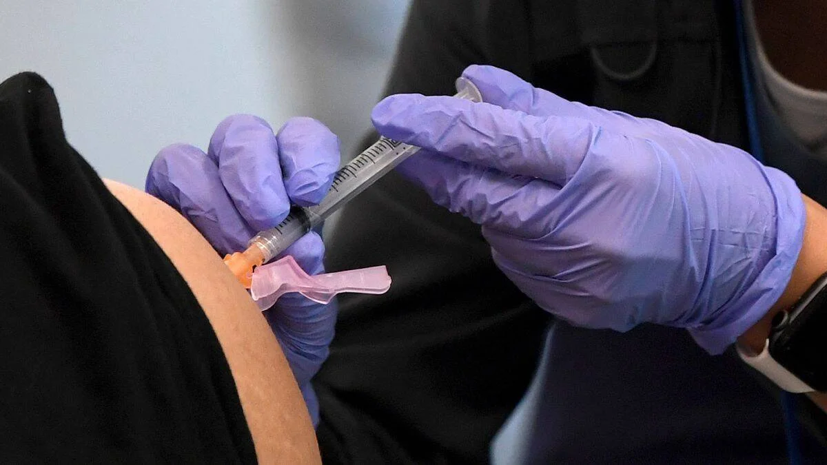 Manos con guantes morados administran una inyección en el brazo de un paciente.